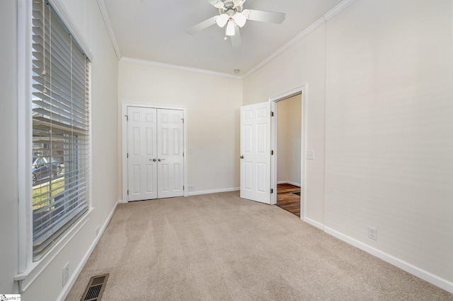 unfurnished bedroom featuring ceiling fan, light colored carpet, a closet, and crown molding