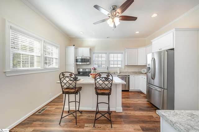 kitchen with stainless steel appliances, light stone countertops, white cabinets, and a center island