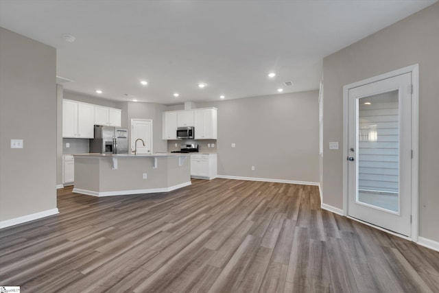 kitchen featuring white cabinetry, light hardwood / wood-style flooring, backsplash, a kitchen island with sink, and appliances with stainless steel finishes