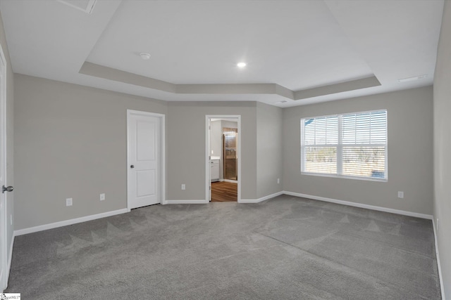 unfurnished bedroom with ensuite bath, light carpet, and a tray ceiling