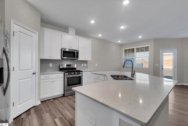 kitchen featuring sink, stainless steel appliances, white cabinets, and a center island with sink