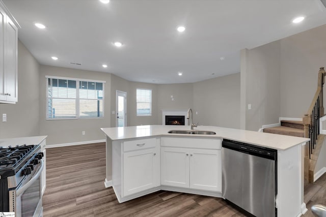 kitchen with a kitchen island with sink, appliances with stainless steel finishes, hardwood / wood-style flooring, sink, and white cabinetry