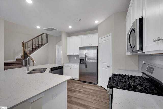 kitchen with stainless steel appliances, light wood-type flooring, light stone counters, sink, and white cabinetry