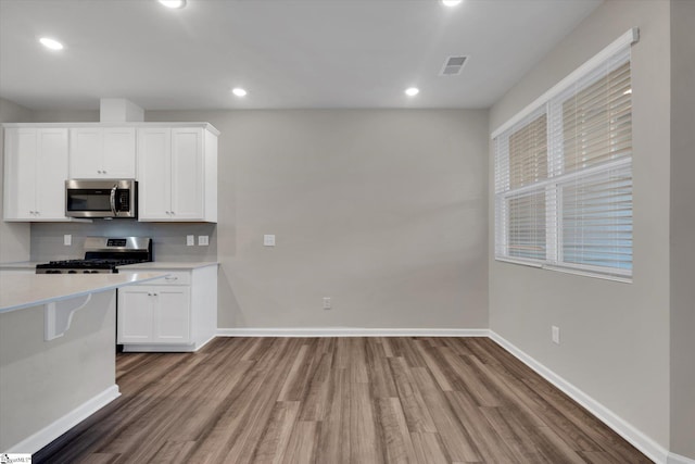 kitchen with appliances with stainless steel finishes, white cabinetry, hardwood / wood-style floors, and tasteful backsplash