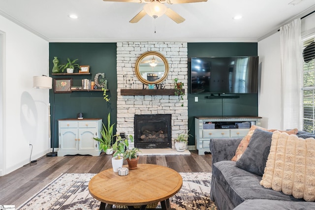 living room with hardwood / wood-style flooring, ceiling fan, crown molding, and a stone fireplace