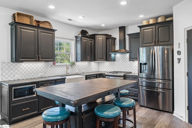 kitchen with stainless steel appliances, light wood-type flooring, wood counters, a kitchen bar, and wall chimney exhaust hood