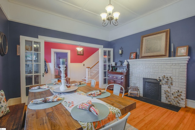 dining room with a brick fireplace, a notable chandelier, wood-type flooring, and ornamental molding