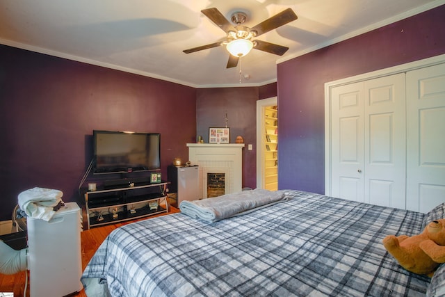 bedroom with a closet, crown molding, ceiling fan, a fireplace, and hardwood / wood-style flooring