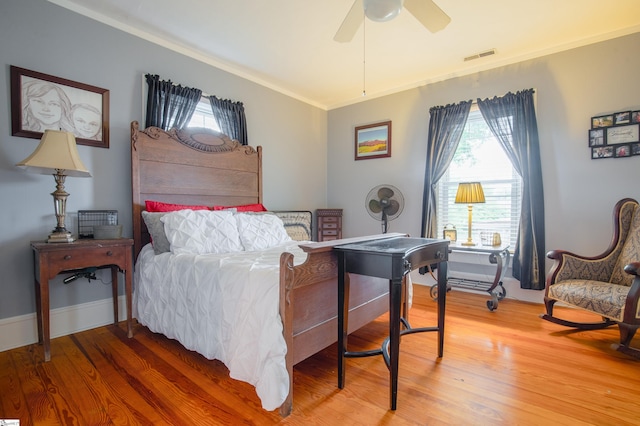 bedroom featuring wood-type flooring, multiple windows, ceiling fan, and ornamental molding