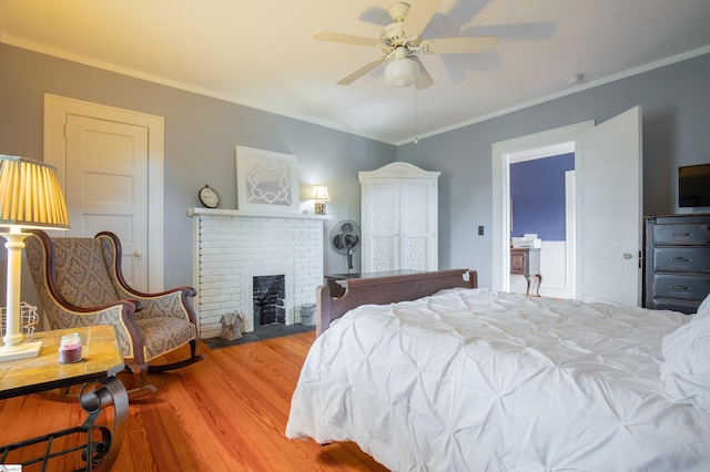 bedroom featuring hardwood / wood-style flooring, ceiling fan, crown molding, and a fireplace