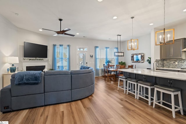 living room featuring sink, ceiling fan with notable chandelier, and light wood-type flooring