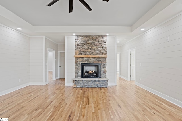 unfurnished living room with wooden walls, a fireplace, ceiling fan, and light hardwood / wood-style flooring