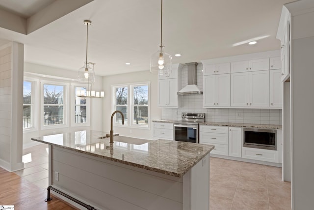 kitchen featuring appliances with stainless steel finishes, hanging light fixtures, an island with sink, wall chimney exhaust hood, and sink