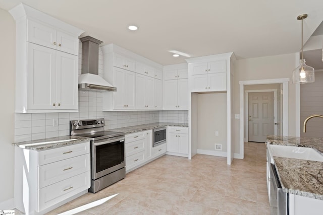 kitchen with stainless steel appliances, wall chimney exhaust hood, white cabinetry, and hanging light fixtures