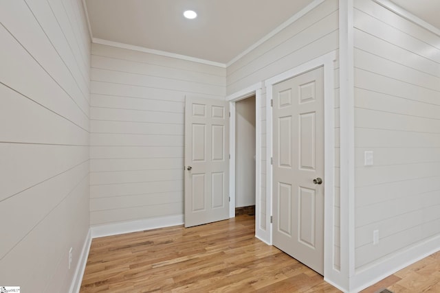 hallway with ornamental molding, light hardwood / wood-style floors, and wooden walls