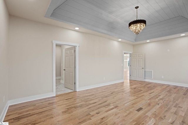 spare room with a raised ceiling, a notable chandelier, light wood-type flooring, and wood ceiling