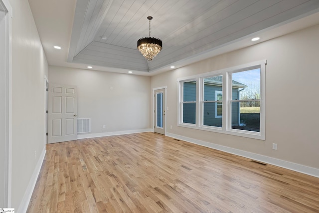 empty room featuring light wood-type flooring, an inviting chandelier, a tray ceiling, and wooden ceiling