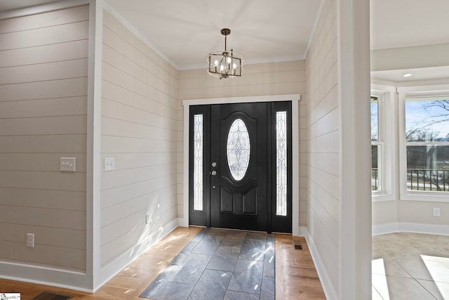 entryway featuring wooden walls, an inviting chandelier, and ornamental molding