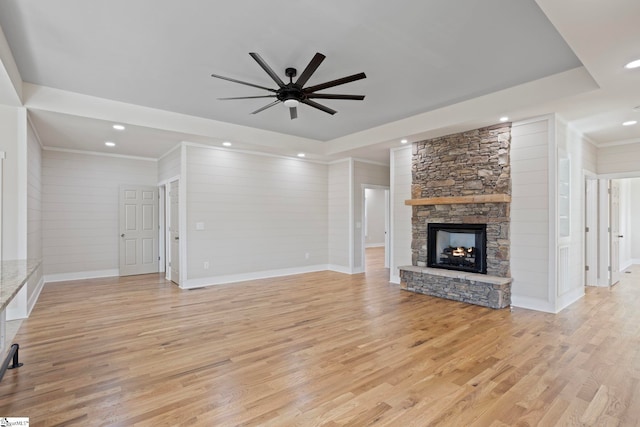 unfurnished living room featuring wooden walls, ceiling fan, light hardwood / wood-style floors, and a stone fireplace