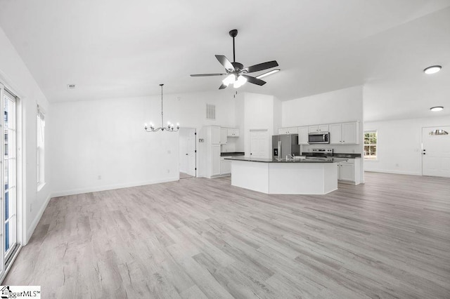 unfurnished living room with ceiling fan with notable chandelier, vaulted ceiling, and light hardwood / wood-style floors