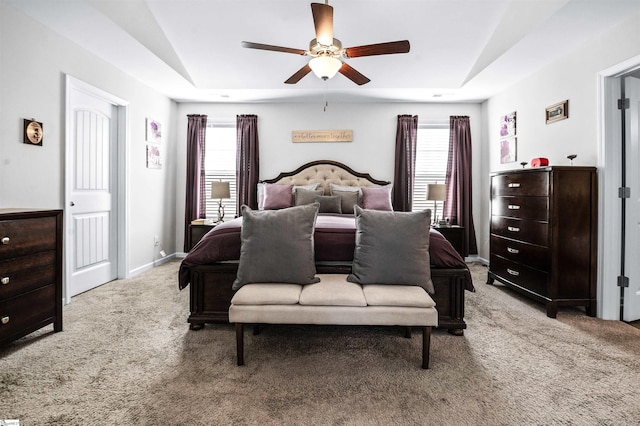 carpeted bedroom featuring ceiling fan, multiple windows, and a raised ceiling