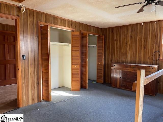 unfurnished bedroom with two closets, a ceiling fan, carpet flooring, wooden walls, and a textured ceiling