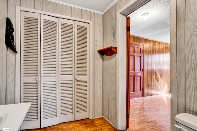 corridor featuring a textured ceiling, wooden walls, crown molding, and wood finished floors