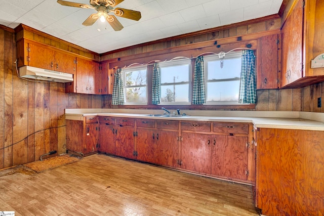 kitchen with under cabinet range hood, a sink, light wood-style floors, light countertops, and brown cabinetry