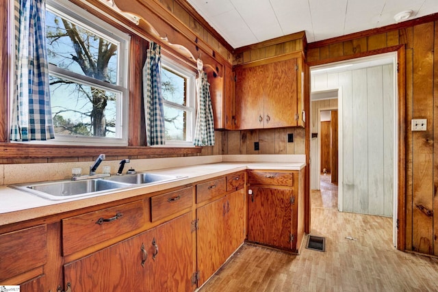 kitchen with wooden walls, a sink, visible vents, light countertops, and brown cabinetry