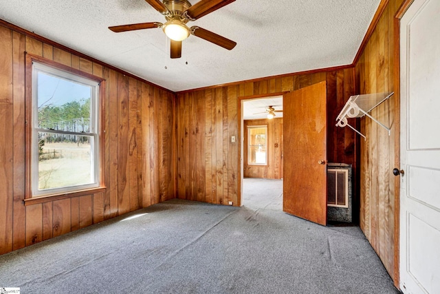 carpeted empty room featuring wooden walls, visible vents, a ceiling fan, crown molding, and a textured ceiling