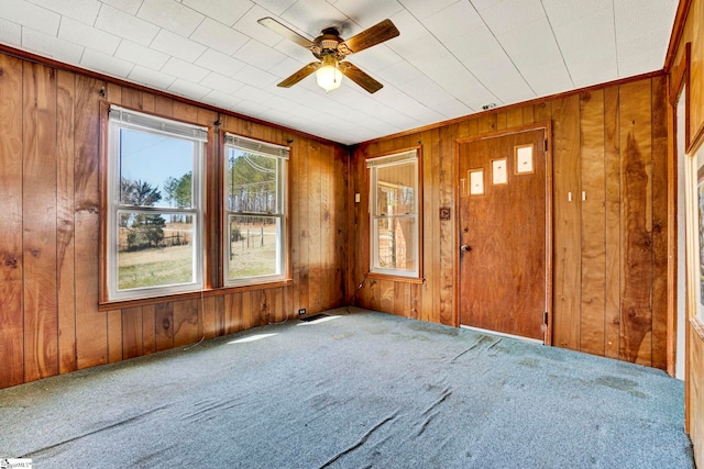 carpeted empty room featuring wood walls and a ceiling fan