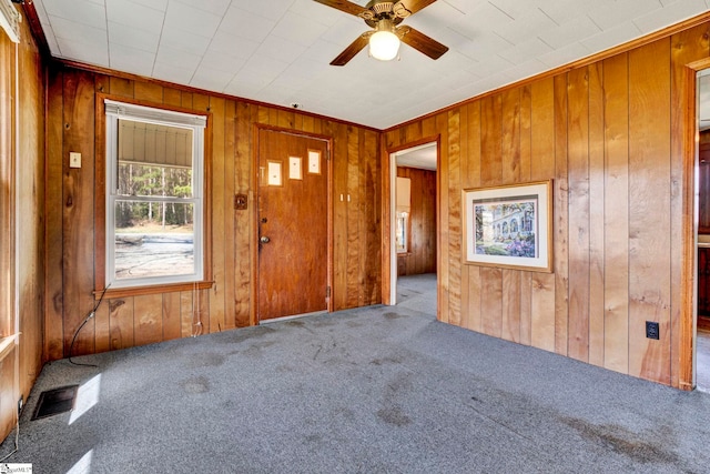 carpeted empty room with wooden walls, visible vents, and a ceiling fan