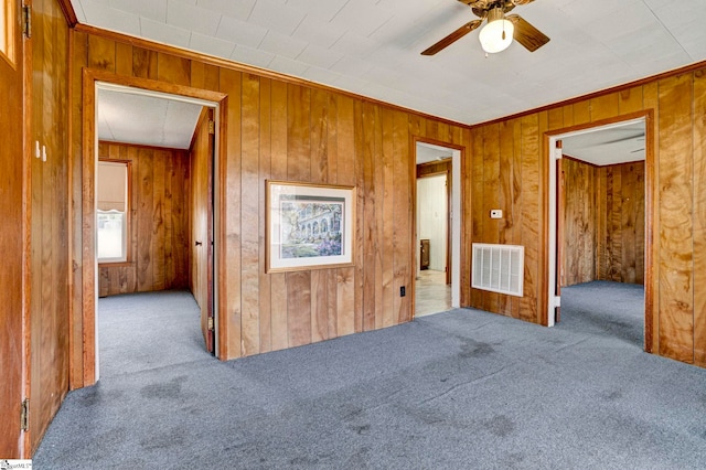 carpeted empty room with wood walls, visible vents, and a ceiling fan