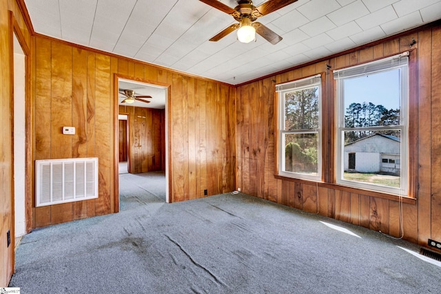 carpeted empty room with ceiling fan, wooden walls, and visible vents