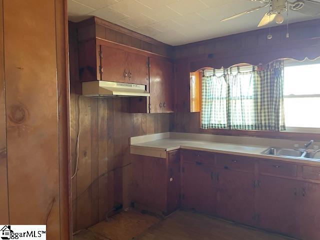 kitchen featuring brown cabinetry, ceiling fan, light countertops, under cabinet range hood, and a sink