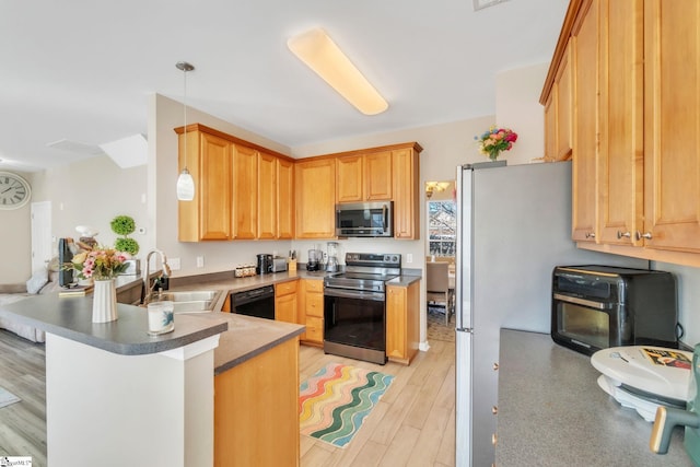 kitchen with stainless steel appliances, sink, light wood-type flooring, kitchen peninsula, and hanging light fixtures