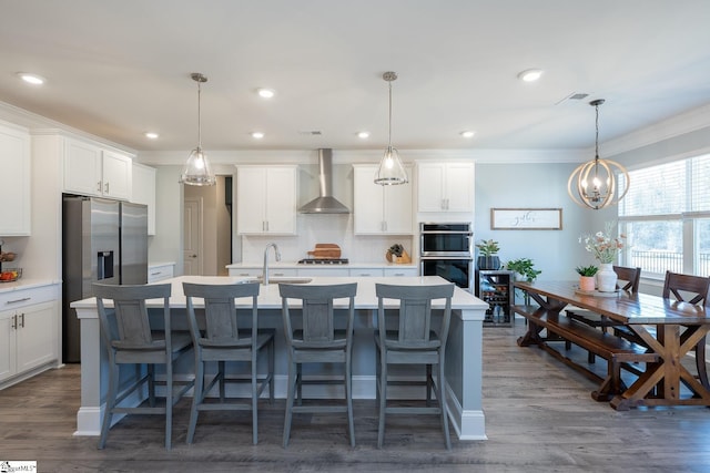 kitchen featuring a center island with sink, decorative light fixtures, white cabinets, and wall chimney range hood