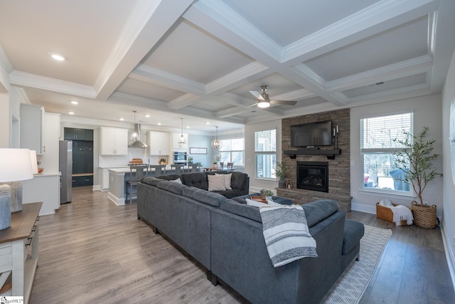 living room with ceiling fan, beamed ceiling, coffered ceiling, light wood-type flooring, and a stone fireplace