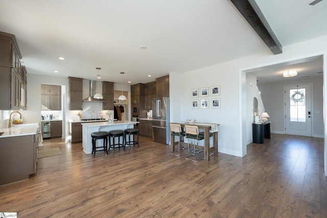 kitchen with high end refrigerator, pendant lighting, a center island, beamed ceiling, and wall chimney exhaust hood