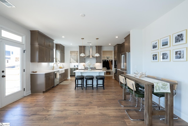 kitchen featuring wall chimney range hood, pendant lighting, an island with sink, a kitchen breakfast bar, and stainless steel appliances