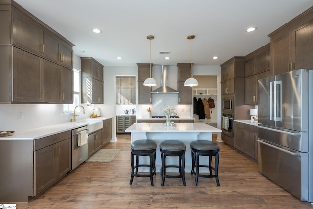 kitchen with decorative light fixtures, sink, dark wood-type flooring, stainless steel appliances, and wall chimney exhaust hood