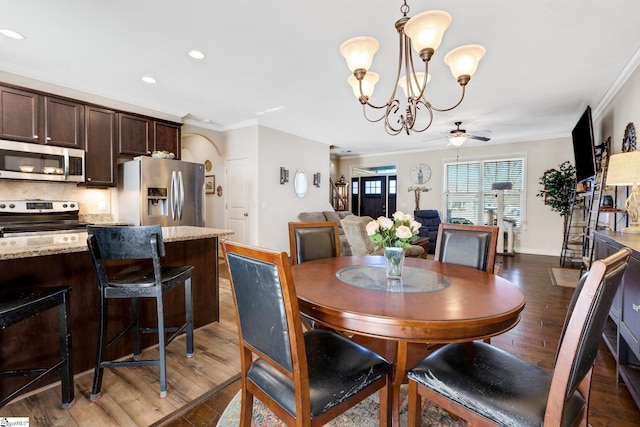 dining room featuring dark wood-type flooring, crown molding, and ceiling fan with notable chandelier