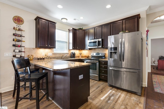 kitchen with appliances with stainless steel finishes, dark brown cabinets, kitchen peninsula, and light stone countertops