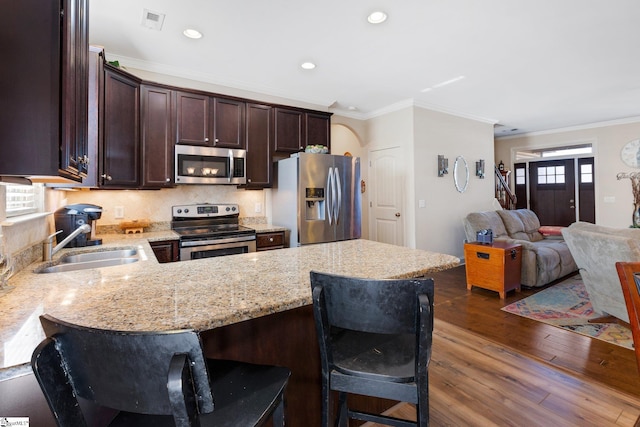 kitchen featuring kitchen peninsula, appliances with stainless steel finishes, crown molding, light stone counters, and sink