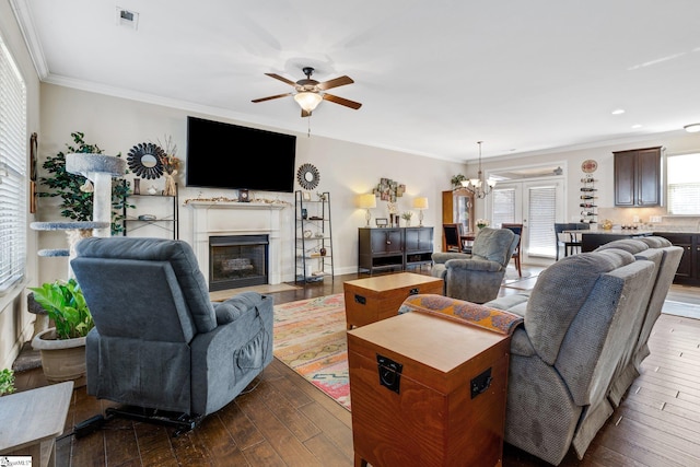 living room with dark hardwood / wood-style flooring, crown molding, and ceiling fan with notable chandelier