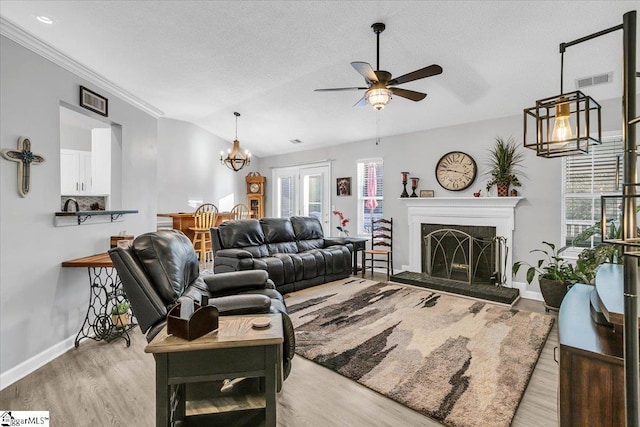 living room featuring lofted ceiling, light hardwood / wood-style flooring, ornamental molding, a textured ceiling, and ceiling fan with notable chandelier