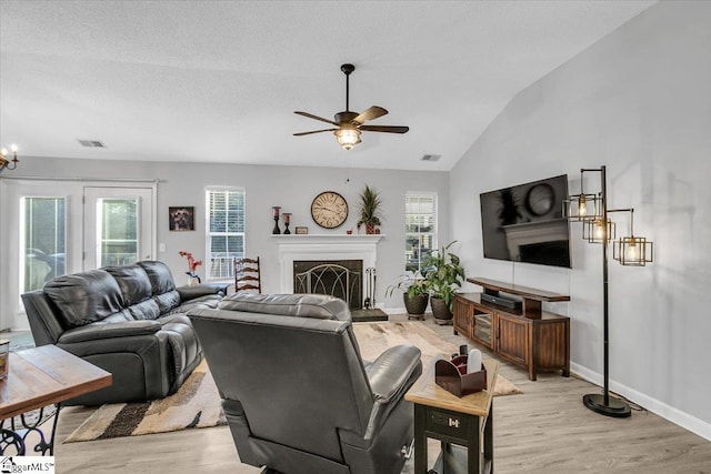 living room featuring lofted ceiling, a fireplace, light hardwood / wood-style flooring, a textured ceiling, and ceiling fan with notable chandelier