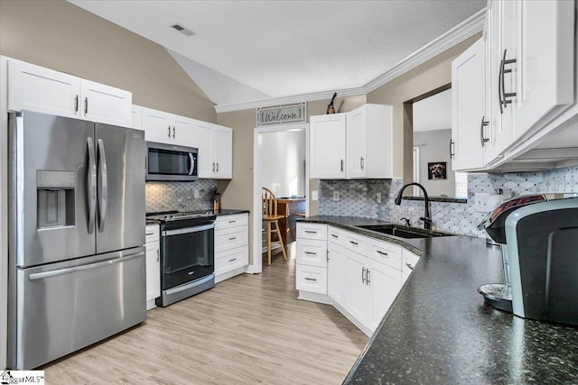 kitchen featuring white cabinetry, appliances with stainless steel finishes, light wood-type flooring, vaulted ceiling, and sink