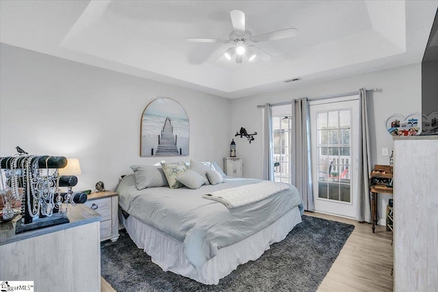 bedroom featuring ceiling fan, hardwood / wood-style flooring, a tray ceiling, and access to exterior