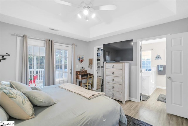 bedroom featuring ceiling fan, a tray ceiling, multiple windows, and light hardwood / wood-style floors